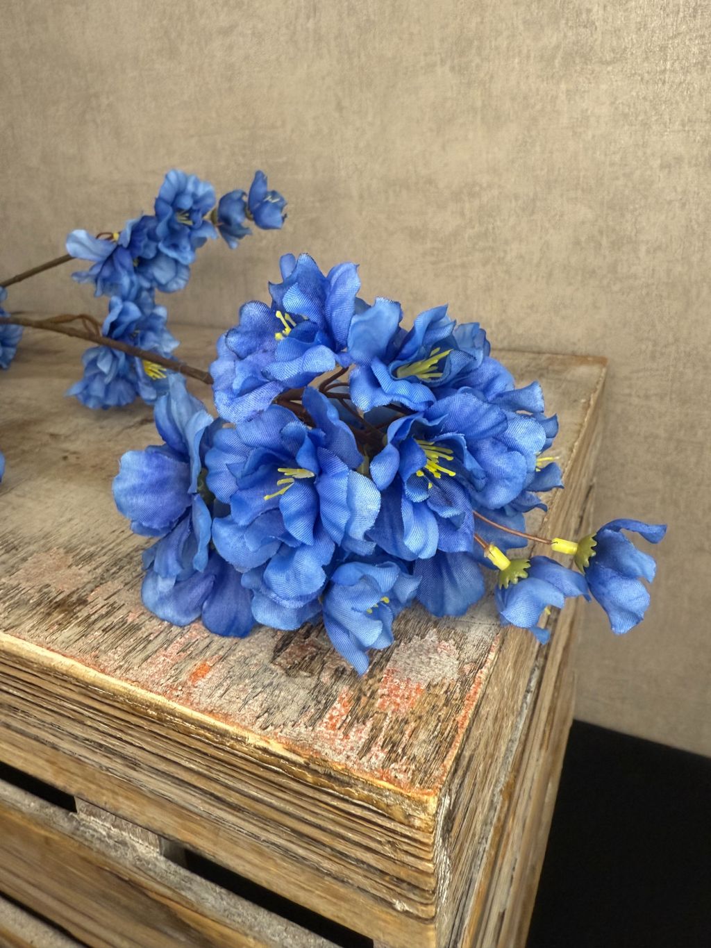 Zijden bloesemtak met helderblauwe bloemen en een fijne vertakking tegen een neutrale achtergrond.