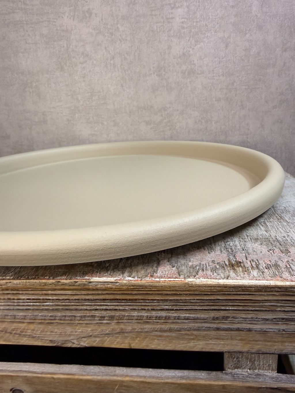 Rond beige metalen dienblad met matte afwerking, geplaatst op een houten ondergrond tegen een neutrale achtergrond.