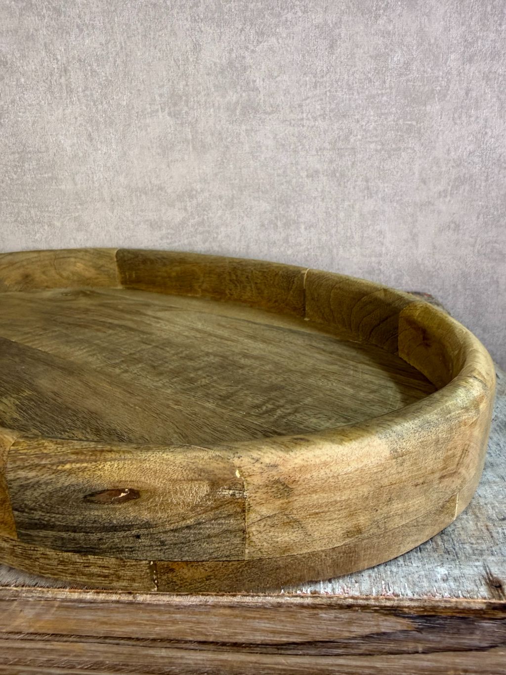 Ovaal houten dienblad met opstaande rand op een houten ondergrond.