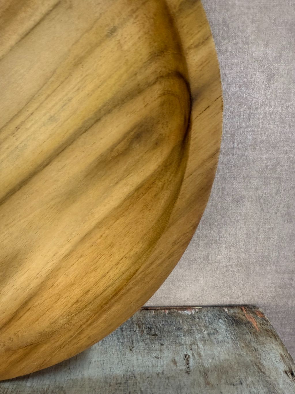 Dienblad Teak – rond houten dienblad van teakhout met natuurlijke nerven op een rustieke ondergrond.