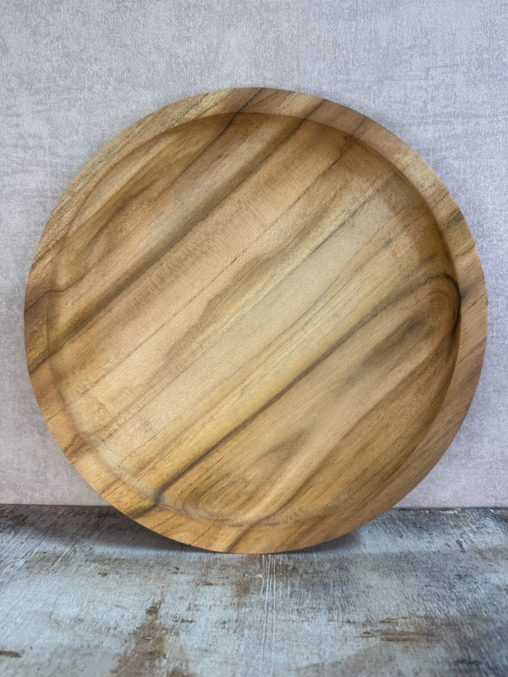 Dienblad Teak – rond houten dienblad van teakhout met natuurlijke nerven op een rustieke ondergrond.