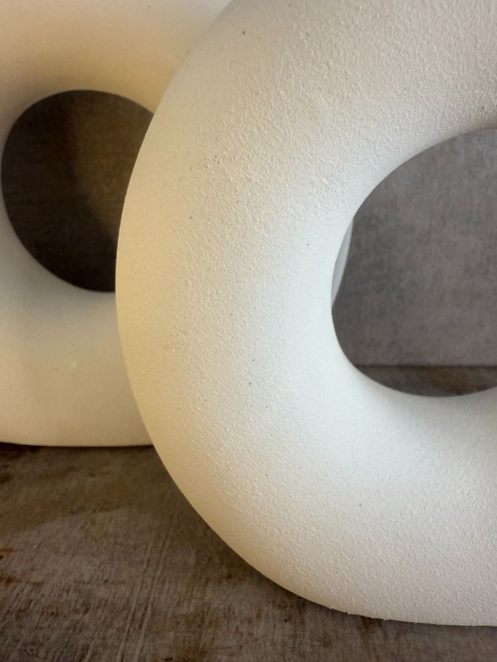 Twee matwitte keramieken donutvazen in Japandi-stijl met ronde openingen, staand op een houten ondergrond tegen een neutrale muur.