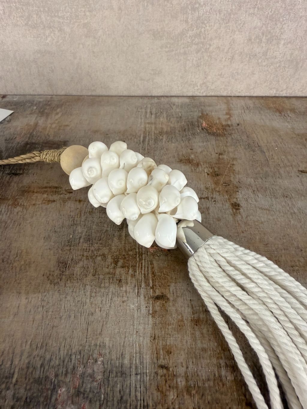 Witte hanger van schelpen en katoen met houten kraal en touw, liggend op een houten ondergrond