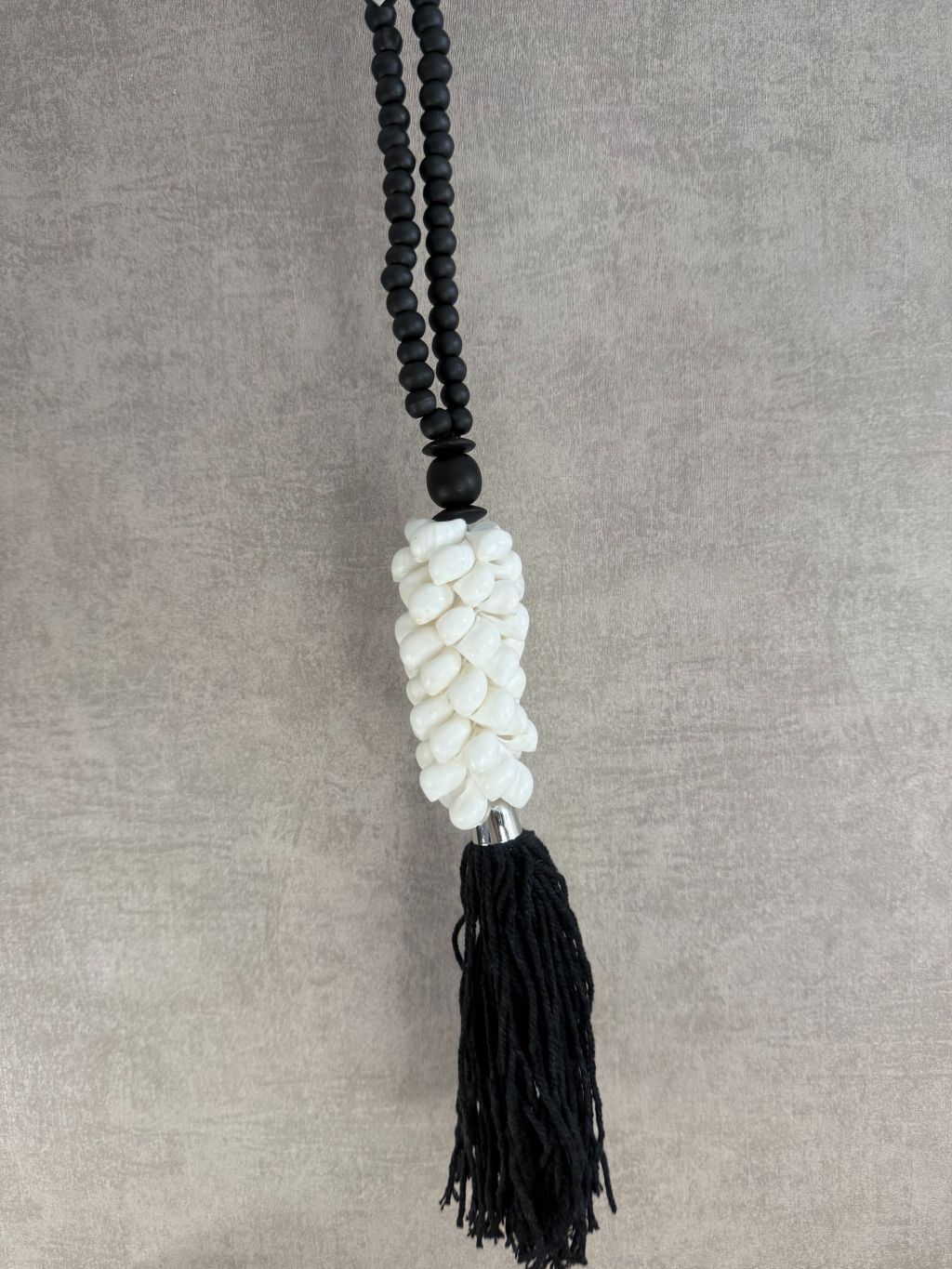 Zwart-witte decoratieve ketting met houten kralen, witte schelpen en zwarte kwast, handgemaakt.