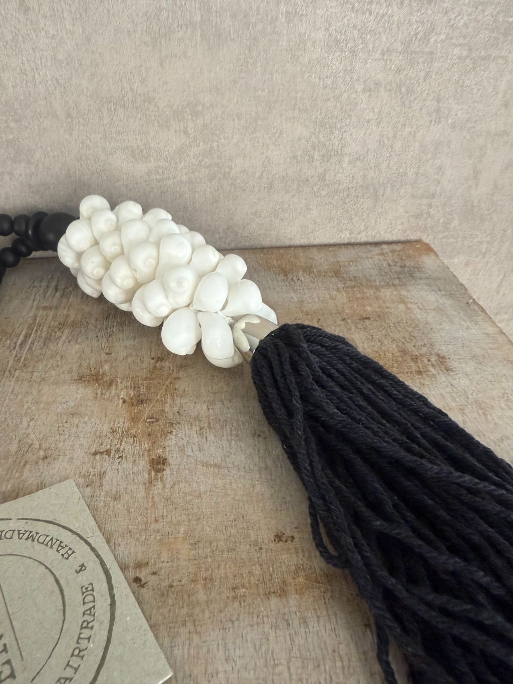 Zwart-witte decoratieve ketting met houten kralen, witte schelpen en zwarte kwast, handgemaakt.