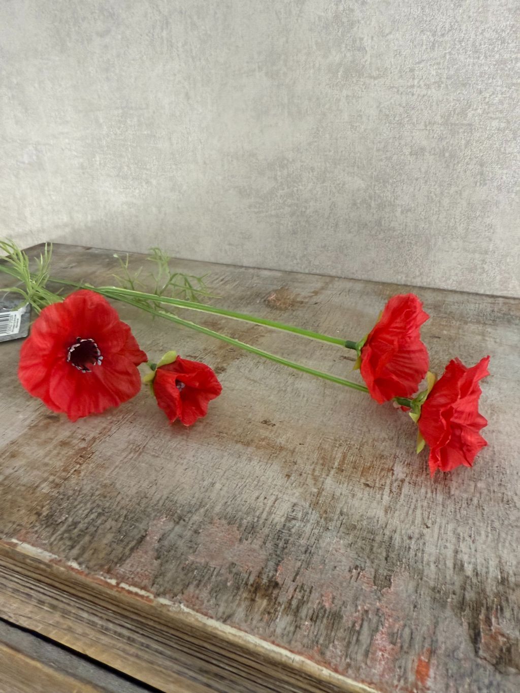 Rode kunstklaproos met drie bloemen en fijne bladeren op houten ondergrond.