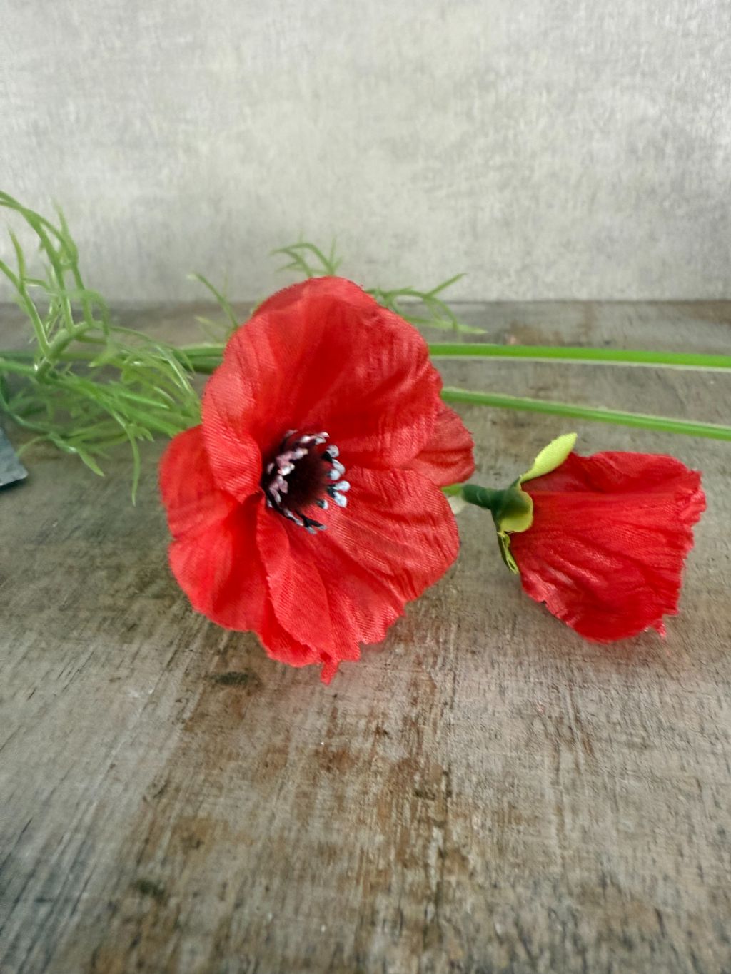 Rode kunstklaproos met drie bloemen en fijne bladeren op houten ondergrond