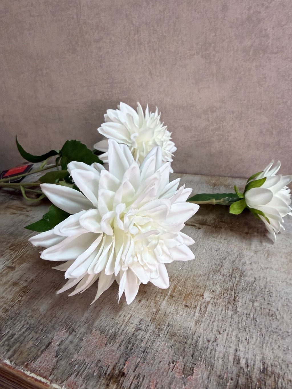 Witte kunstbloem chrysant met volle bloemblaadjes en groene steel, liggend op een houten ondergrond.