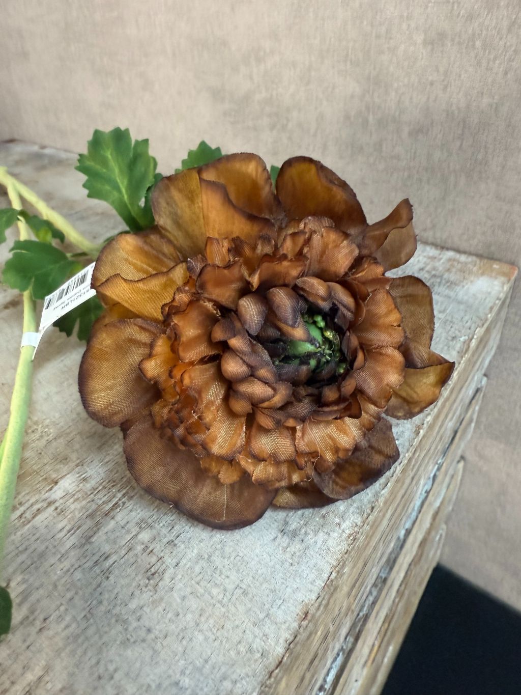 Bruine kunstbloem dahlia met lange steel en groene bladeren op een houten kist dichtbij.