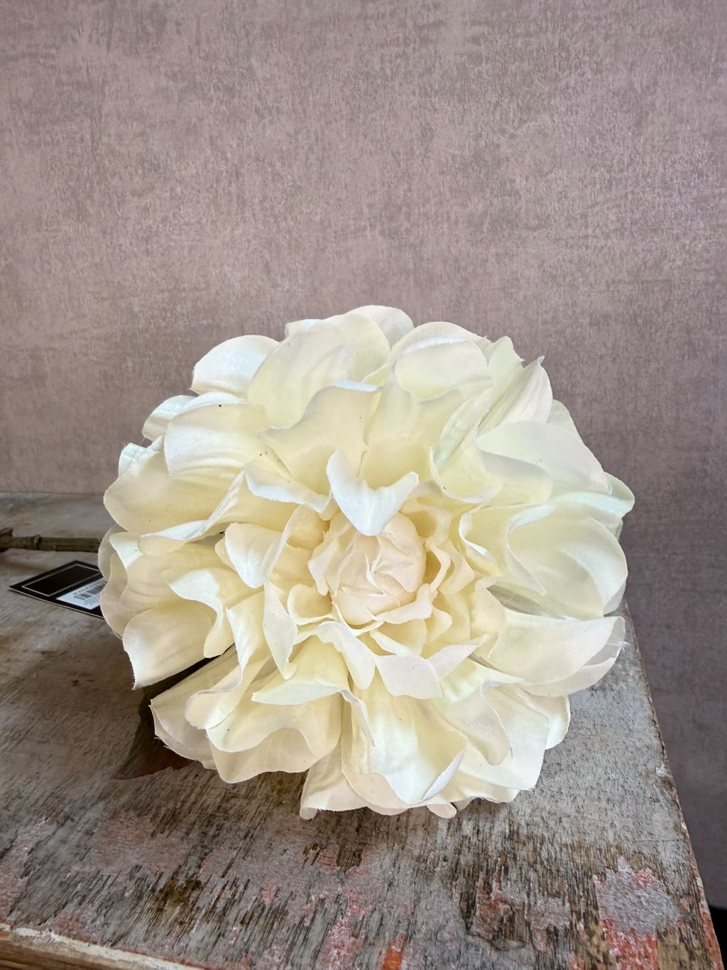 Crèmekleurige kunstbloem dahlia met volle bloem en groene bladeren tegen een neutrale achtergrond.