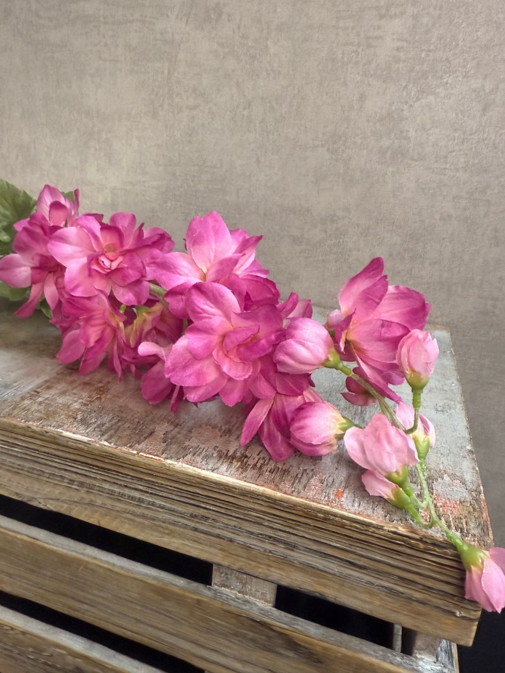 Roze kunstbloem Delphinium Cherise met volle bloei en lange steel, liggend op een houten krat
