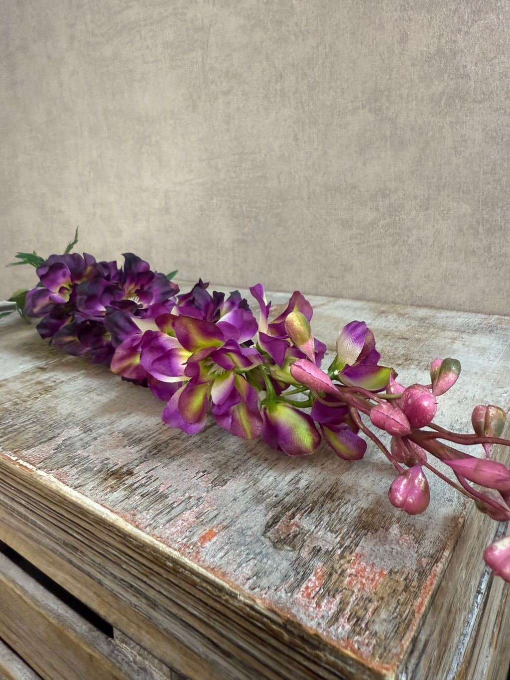 Kunstbloem Delphinium Paars melange met paarse bloemen en groene steel, liggend op een grijze ondergrond.