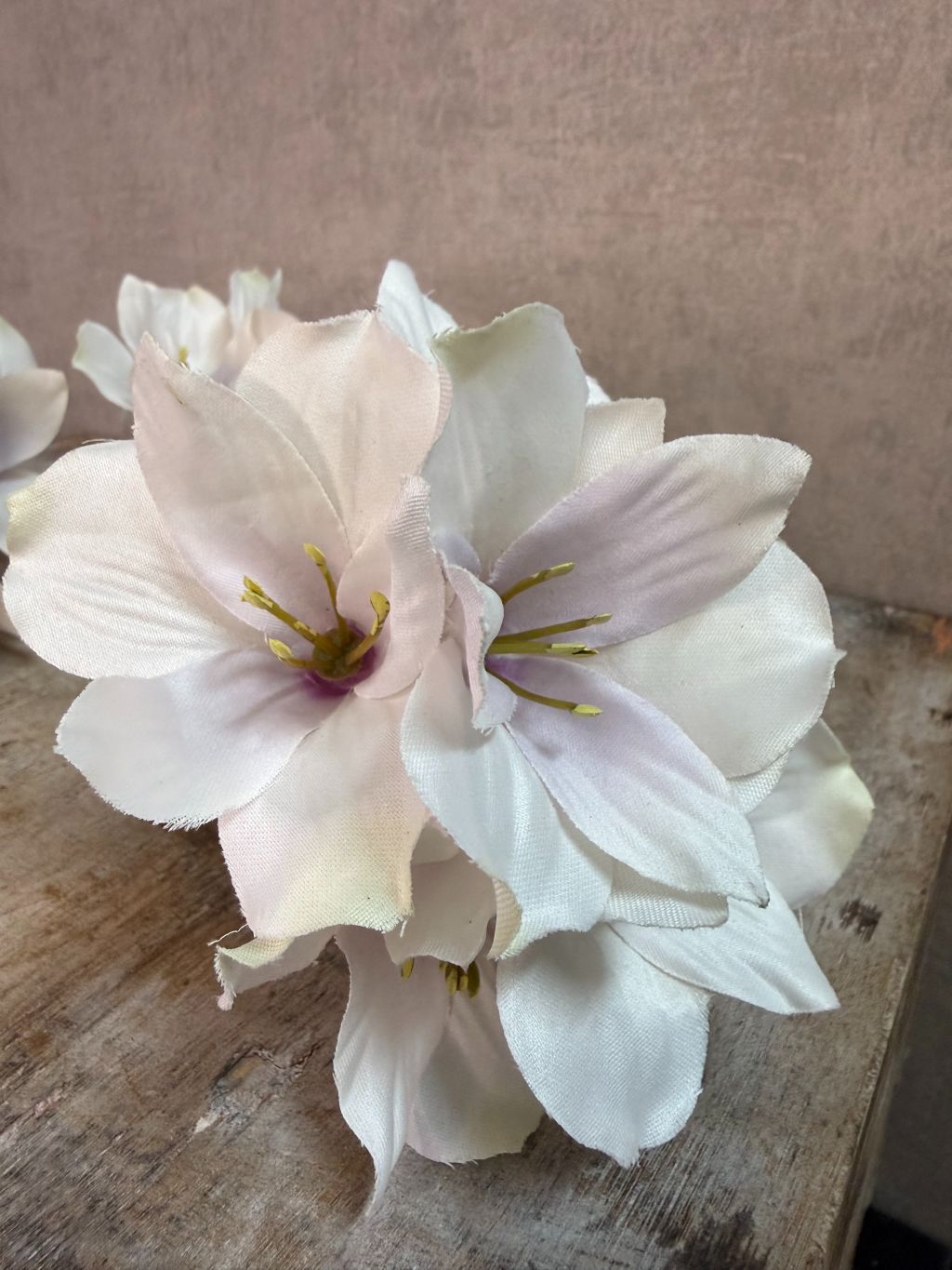 Kunstmatige hibiscus bloem in crème roze tinten met meerdere bloesems op een steel tegen een neutrale achtergrond.