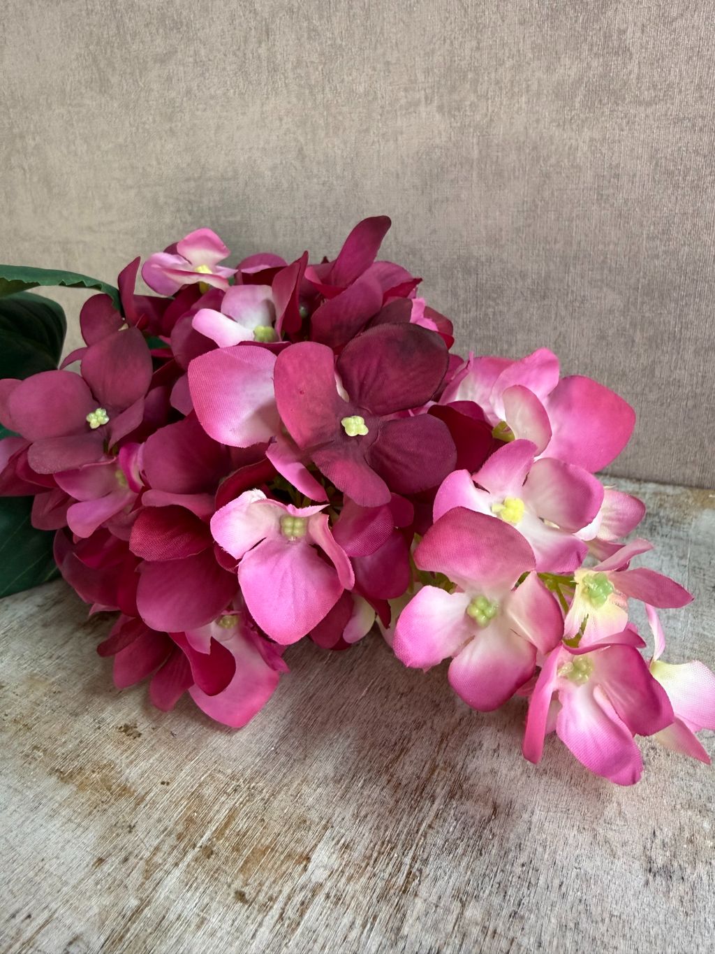 Kunstbloem hortensia in cherry red met volle bloemtros en roze-rode kleurschakering, liggend op een houten ondergrond.