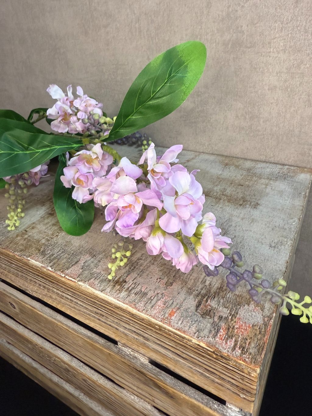 Kunstbloem lupine in lila tint met lange groene steel en bladeren op een houten kist/