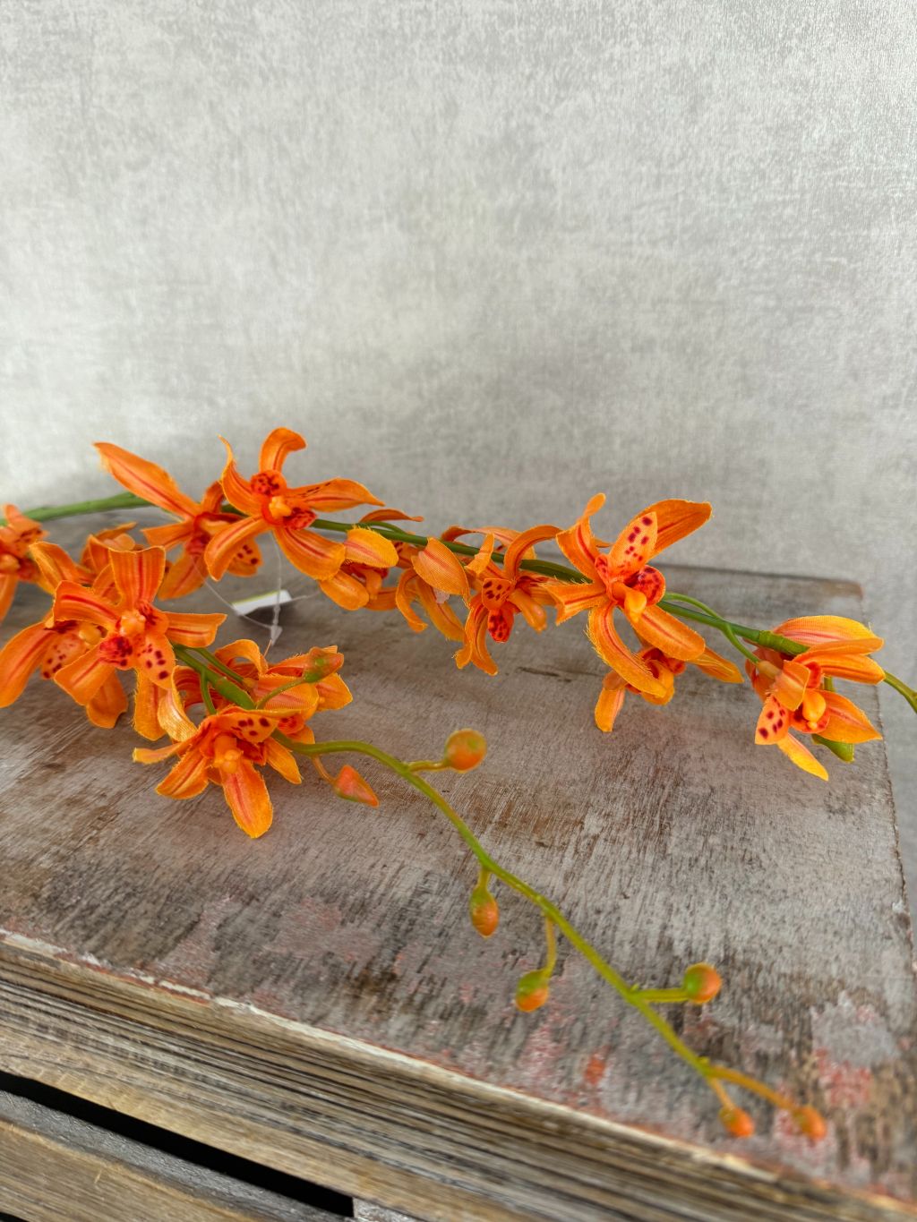 Oranje kunstorchidee met lange steel en realistische bloemen tegen houten ondergrond