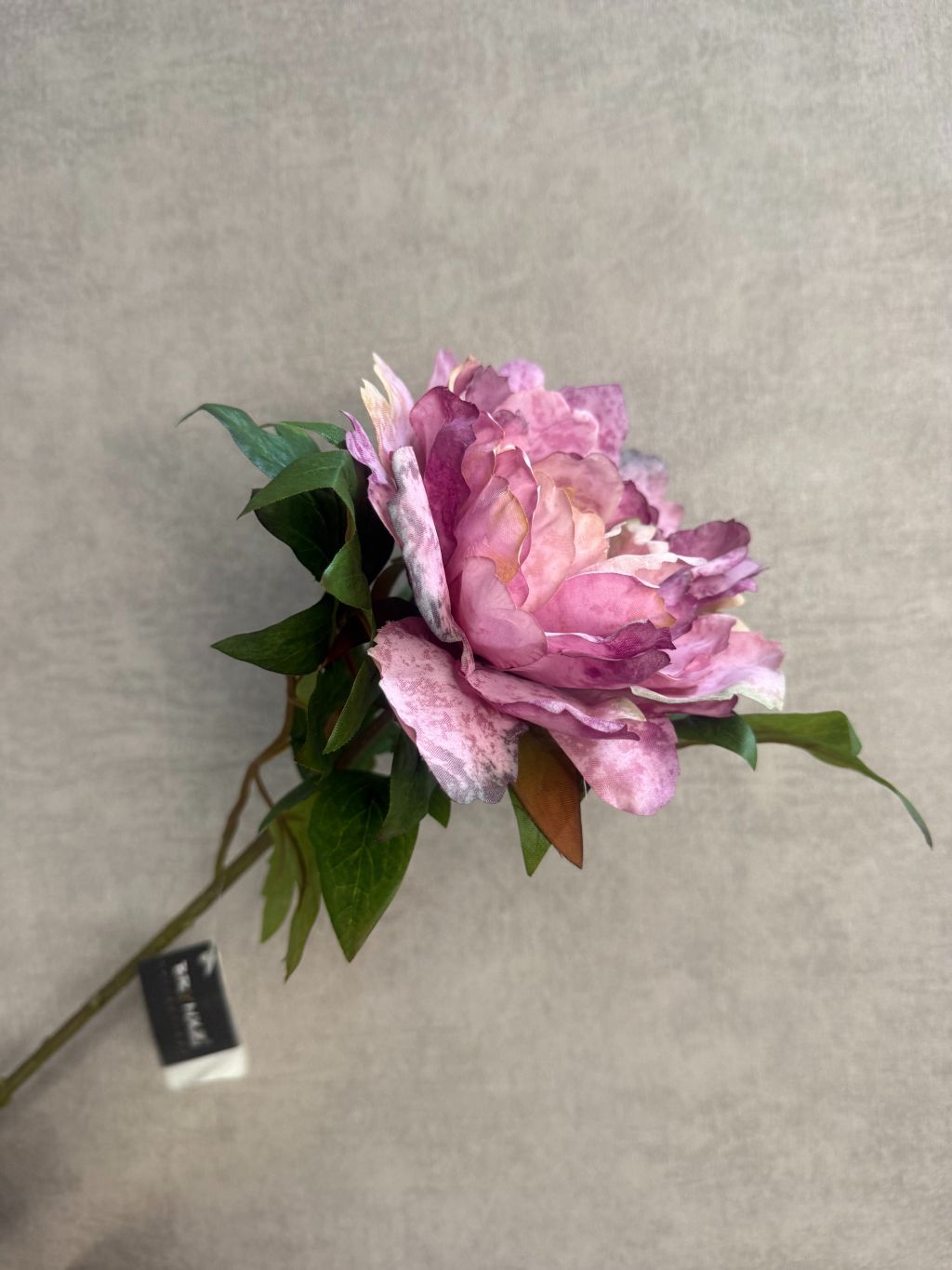 Kunstbloem pioen in paars melange, liggend op een houten ondergrond met zichtbare bladeren.