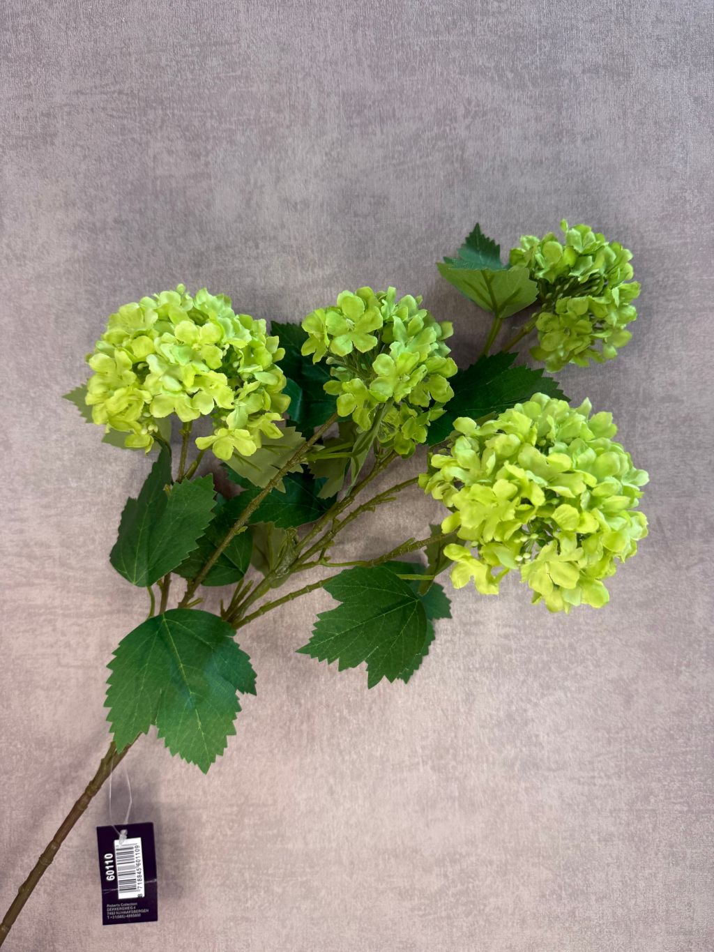 Kunstbloem sneeuwbal met meerdere groene bolvormige bloemkoppen en getande bladeren tegen een neutrale achtergrond.