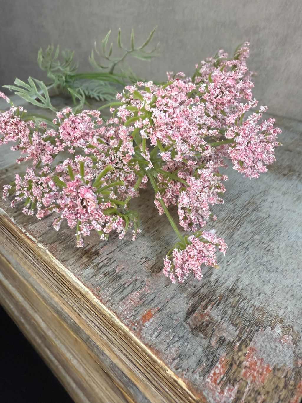 Close-up van een kunstbloem Wilde peen in zachte roze tint, liggend op een houten ondergrond met vintage uitstraling.