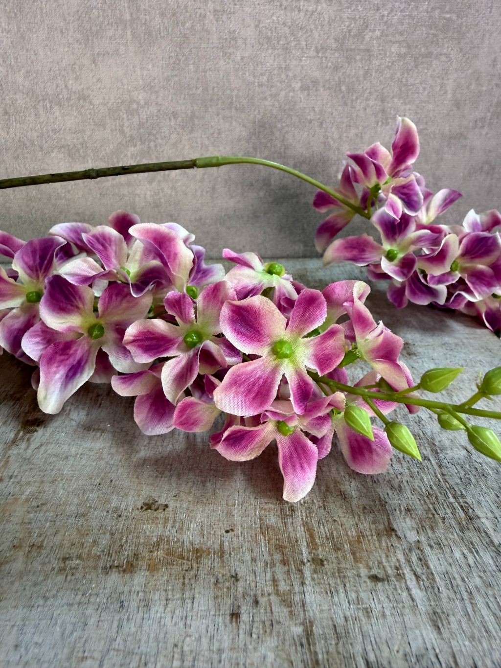 Paars roze kunstbloem Wisteria met hangende bloemtrossen en groene steel op een neutrale achtergrond.