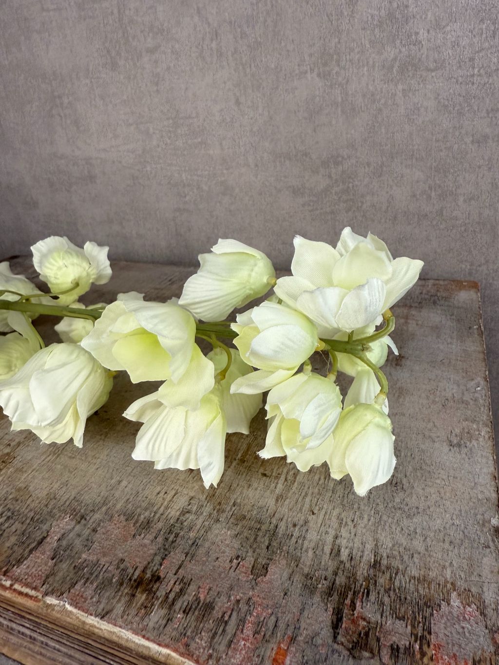 Crèmekleurige kunstbloem Campanula met klokvormige bloemen en groene bladeren tegen een neutrale achtergrond.