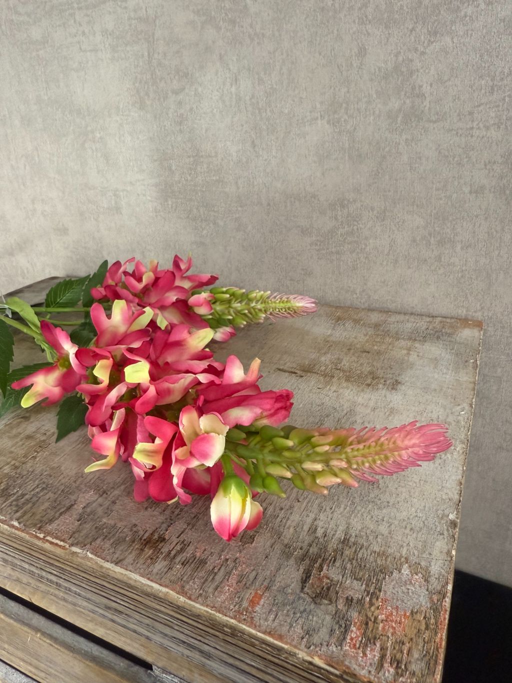 Kunstbloem lupine in fuchsia met groene bladeren en dubbele bloemtros, gefotografeerd tegen een neutrale grijze achtergrond.