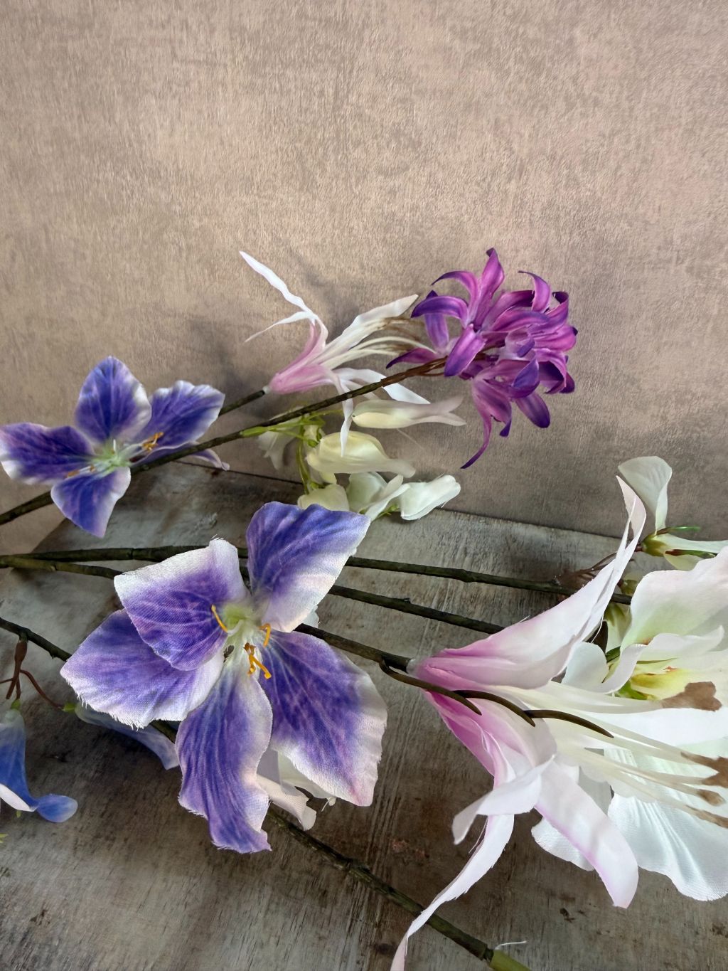 Extra lange kunstbloem met gemengde bloemen in wit, blauw en paars, liggend op een neutrale achtergrond.