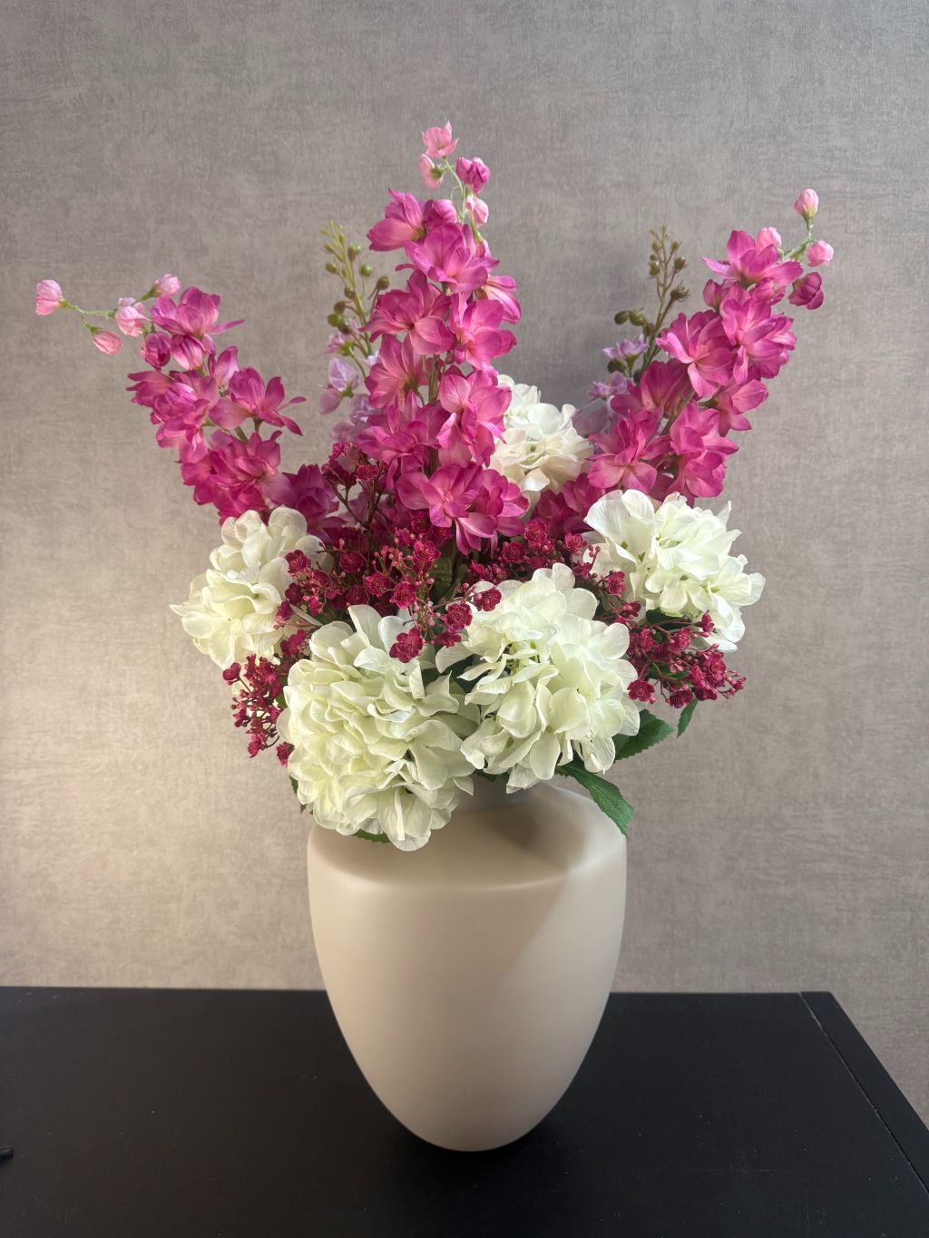 Kunstboeket Cherise met witte hortensia’s en fuchsia bloemen in ivoorkleurige vaas tegen neutrale achtergrond.