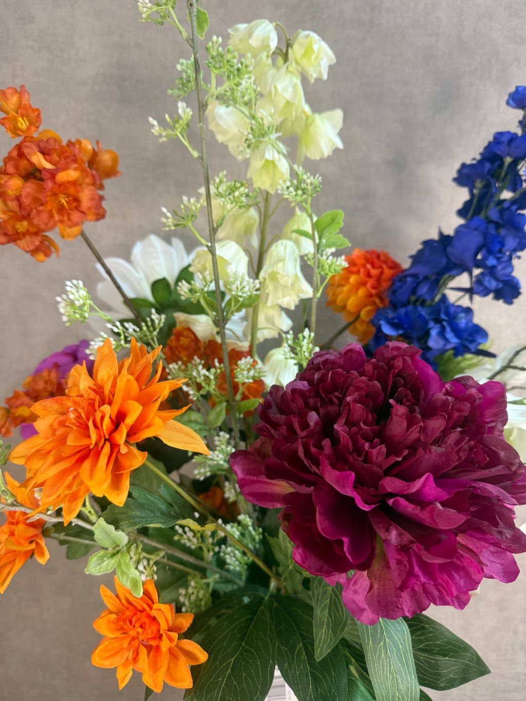 Kunstboeket met kleurrijke bloemen in beige vaas, waaronder pioenroos, dahlia en campanula.