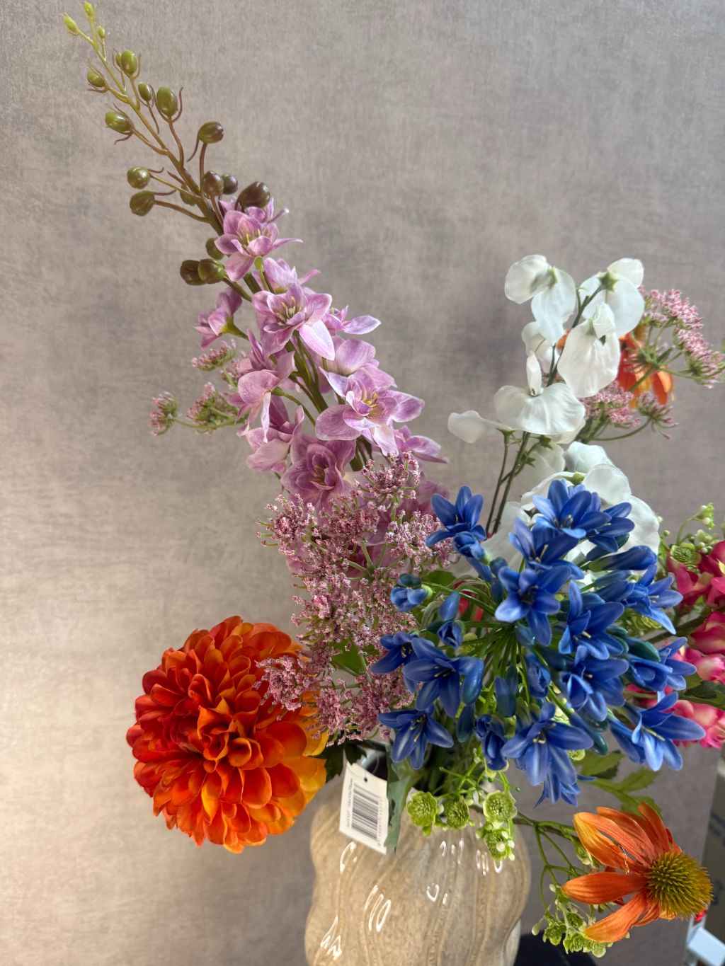 Kunstboeket met gemengde bloemen in diverse kleuren, geplaatst in een golvende beige vaas op zwarte ondergrond.