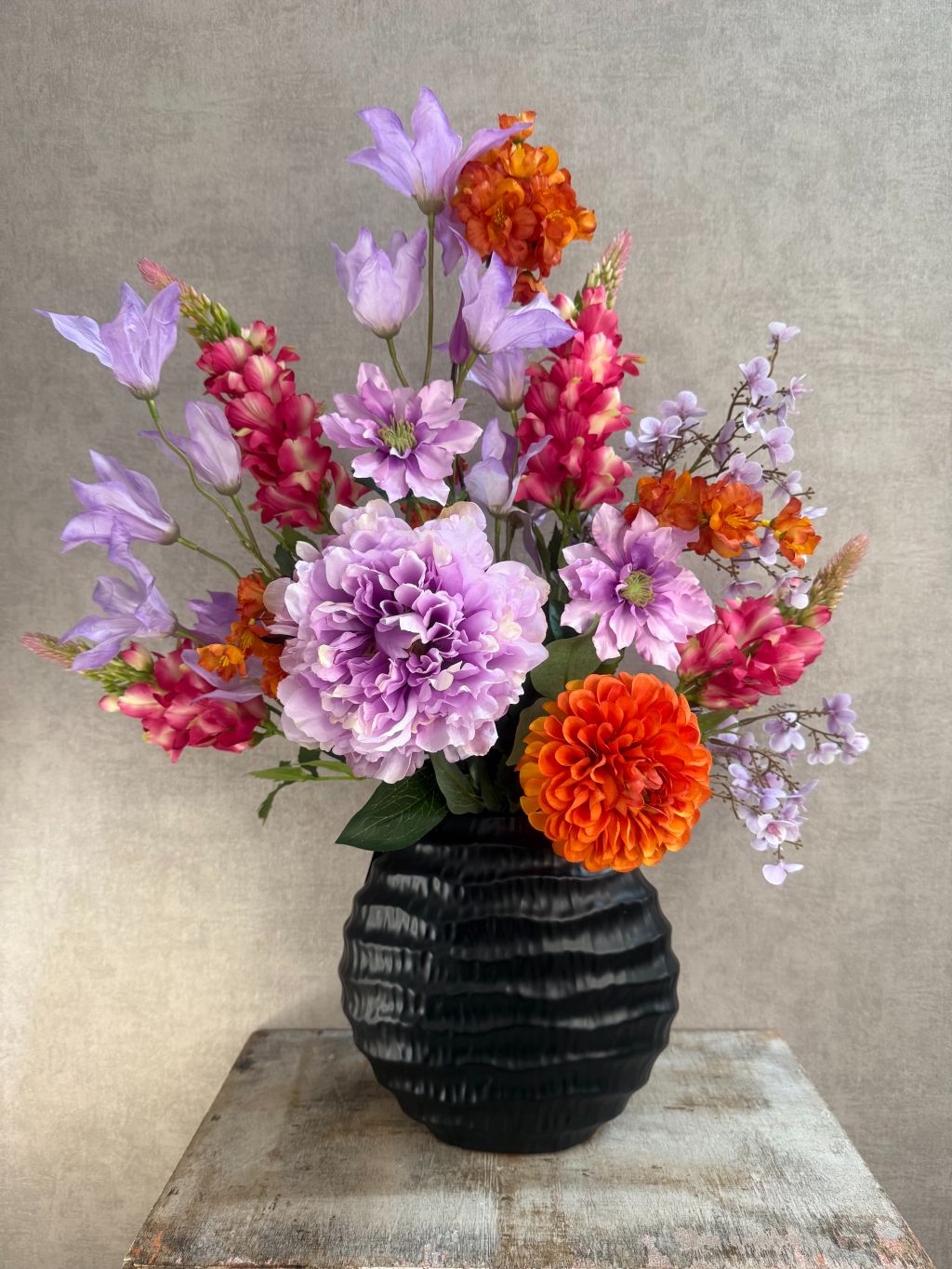 Kunstboeket in zwarte vaas met paarse, roze en oranje bloemen, front-facing geschikt voor vensterbank of wandmeubel.