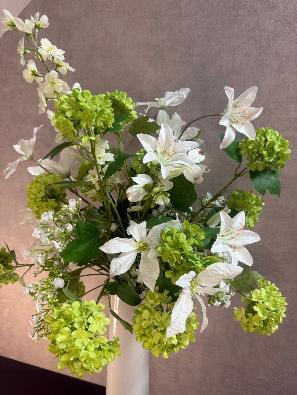 Kunstboeket met witte bloemen en groene sneeuwballen in een hoge crème vaas op zwarte ondergrond.