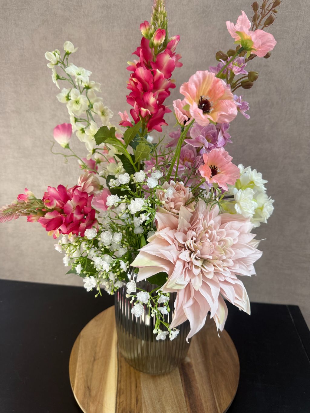 Kunstboeket Lovey met paarse, roze en witte bloemen in geribbelde glazen vaas op ronde houten onderzetter.