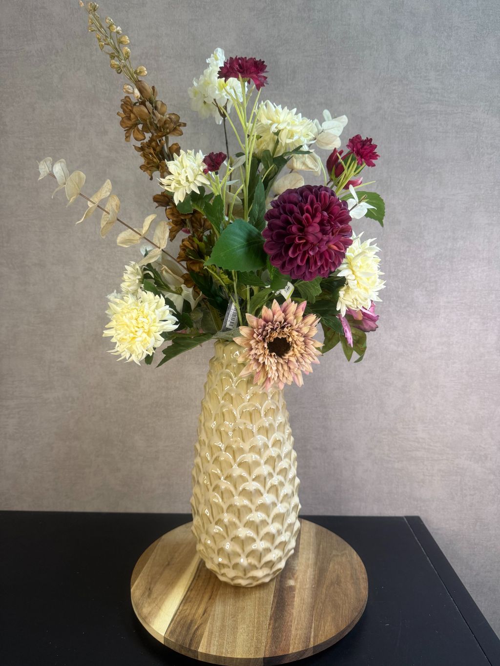 Kunstboeket Noëlle – volle bos kunstbloemen in beige, bruin en bordeaux tinten in een beige vaas tegen grijze achtergrond.