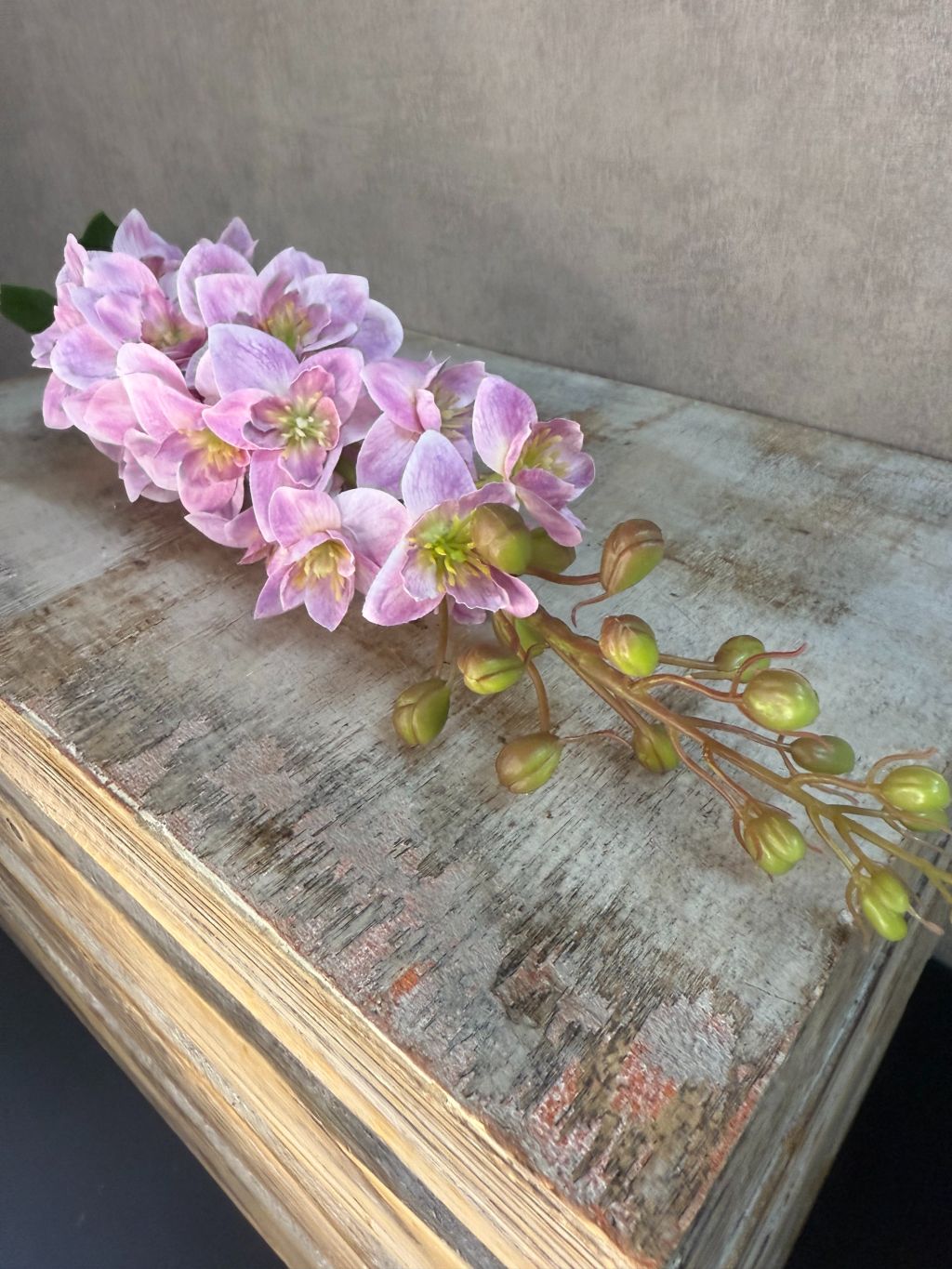 Kunstbloem Delphinium in lila/roze tinten met een volle bloeiwijze en groene steel, liggend op een houten ondergrond.
