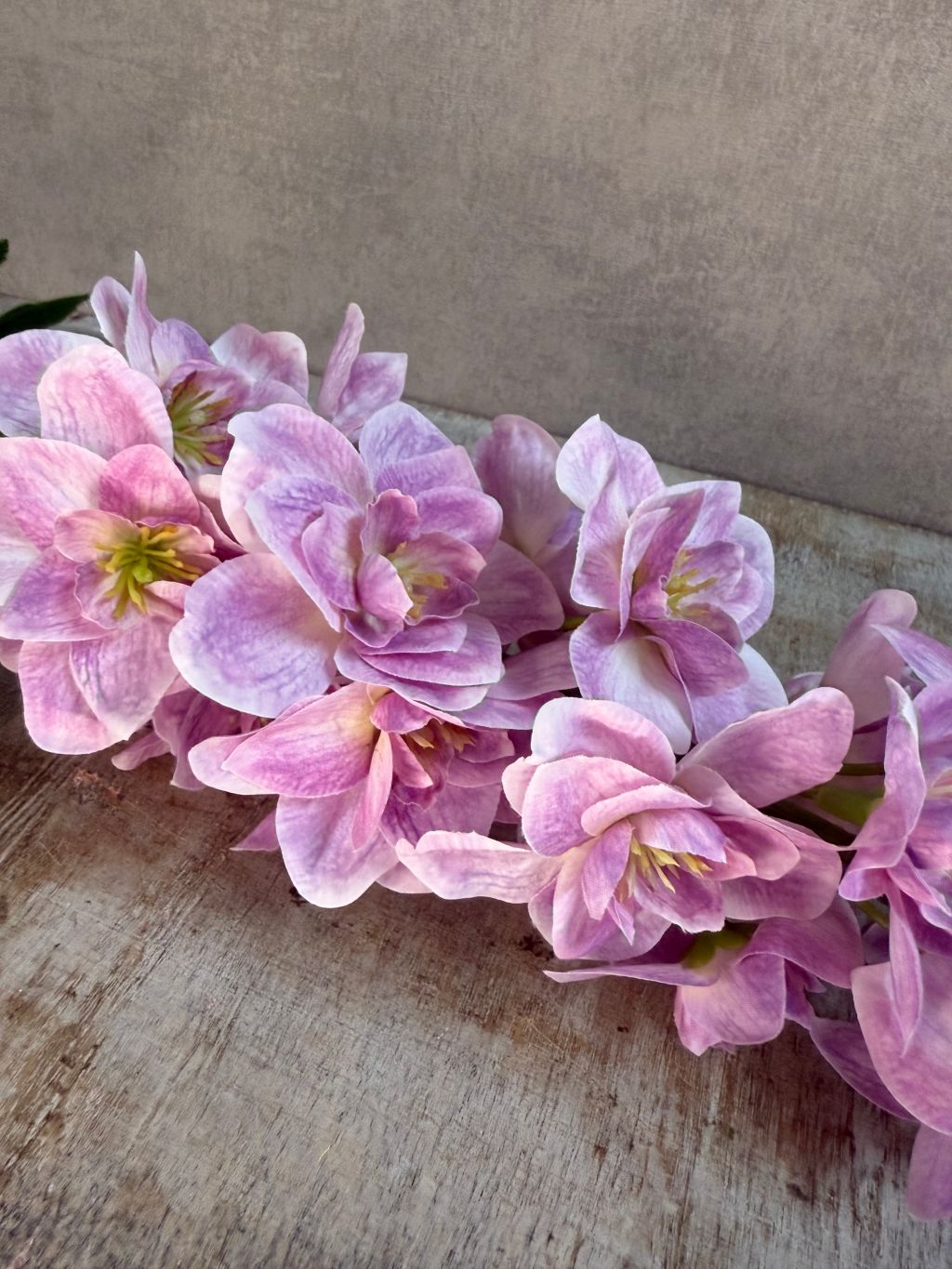 Kunstbloem Delphinium in lila/roze tinten met een volle bloeiwijze en groene steel, liggend op een houten ondergrond.