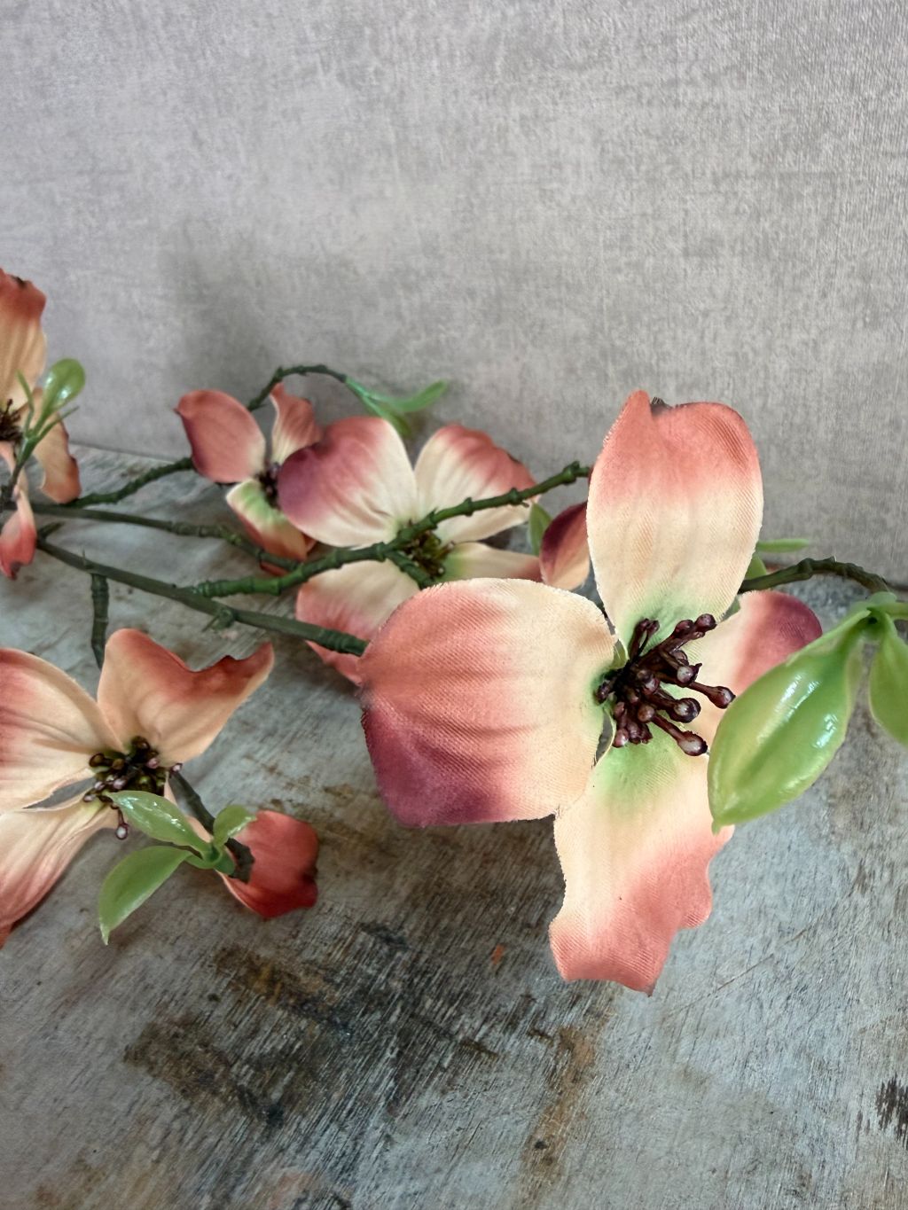 Kunsttak met bruine en crème bloesems en groene knoppen tegen een neutrale achtergrond.