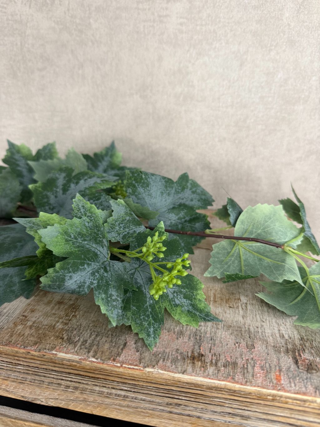 Kunsttak druivenblad van 77 cm met grote groene bladeren en fijne details op houten ondergrond