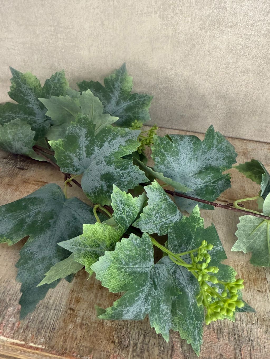 Kunsttak druivenblad van 77 cm met grote groene bladeren en fijne details op houten ondergrond