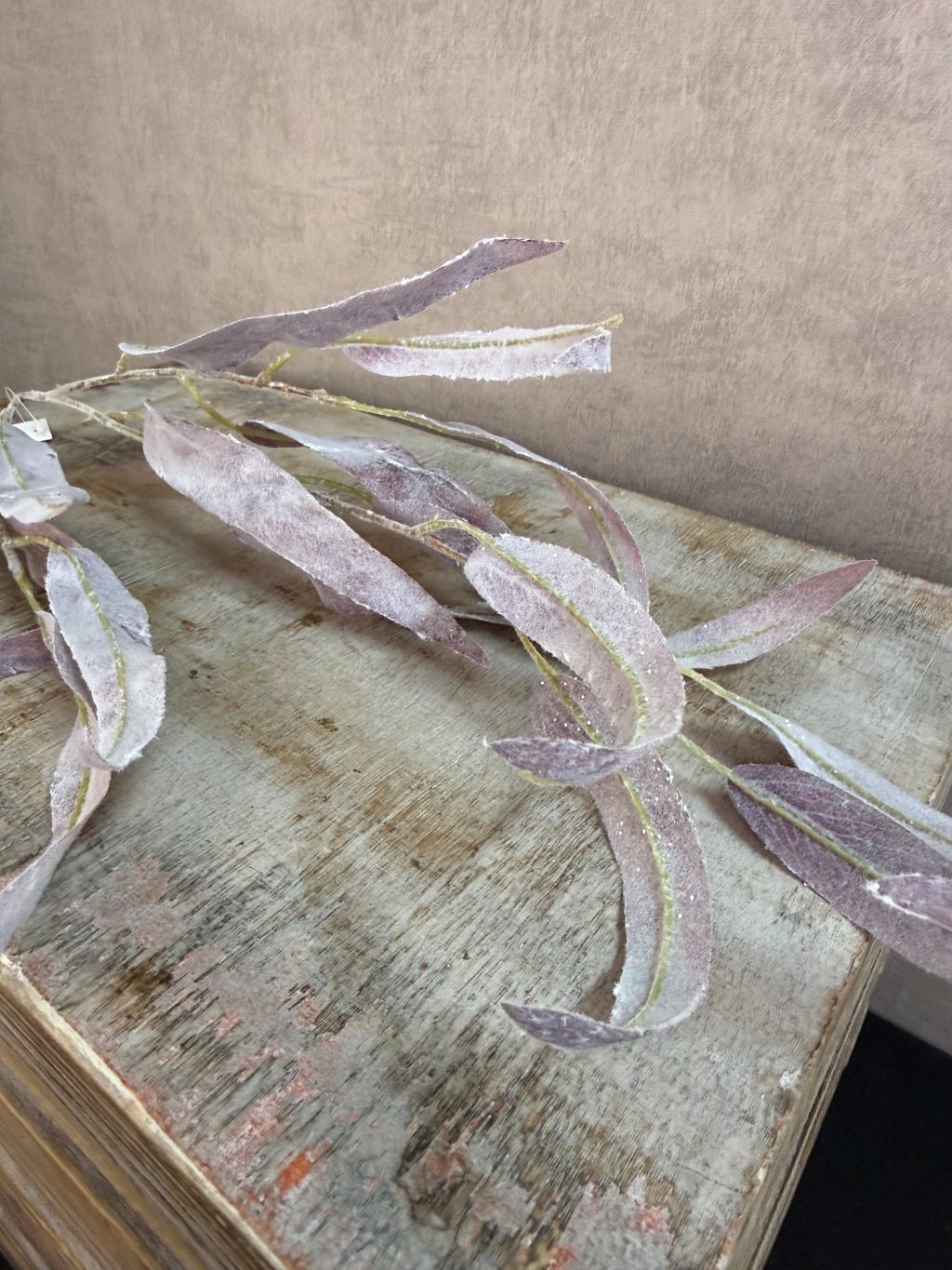 Paarse kunsttak eucalyptus met slanke bladeren en subtiele glitter tegen een neutrale achtergrond.