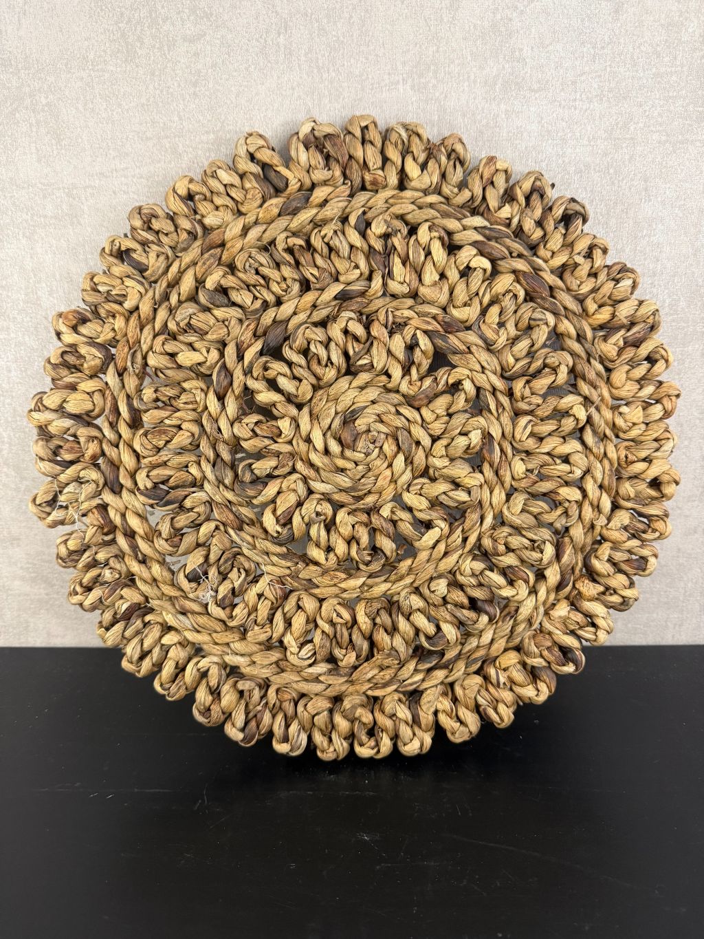 Ronde handgemaakte placemat van grof gevlochten raffia in warme bruintinten met decoratieve rand.