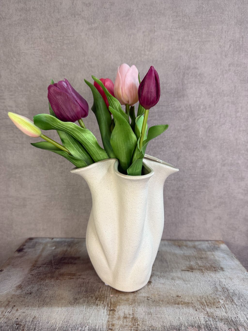 Bos real touch tulpen in paars- en rozetinten met groene bladeren, liggend op een houten ondergrond tegen een neutrale achtergrond.