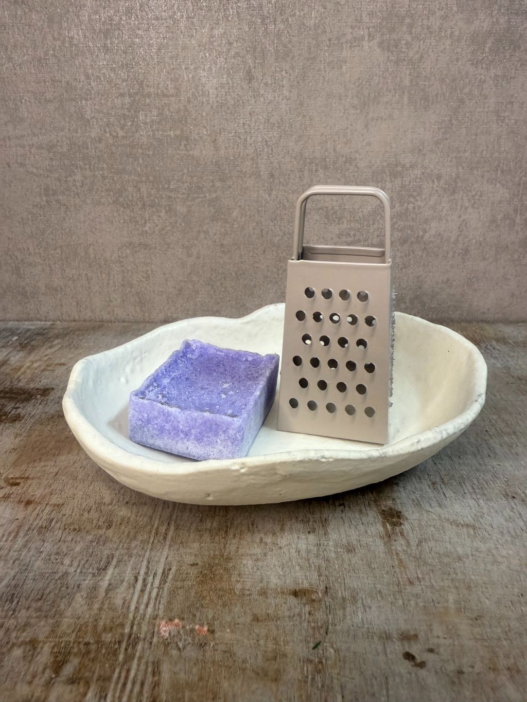 Crèmekleurig keramieken schaaltje met organische, golvende rand, geplaatst op een houten met een amberblokje en rasp