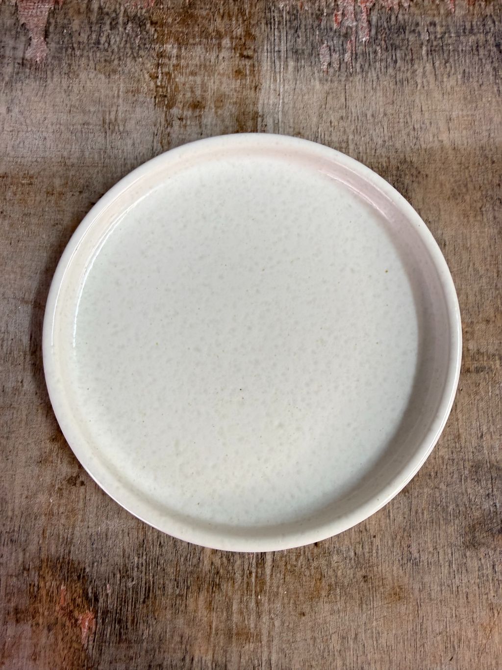 Wit keramieken schaaltje met opstaande rand op een houten ondergrond tegen een neutrale achtergrond.