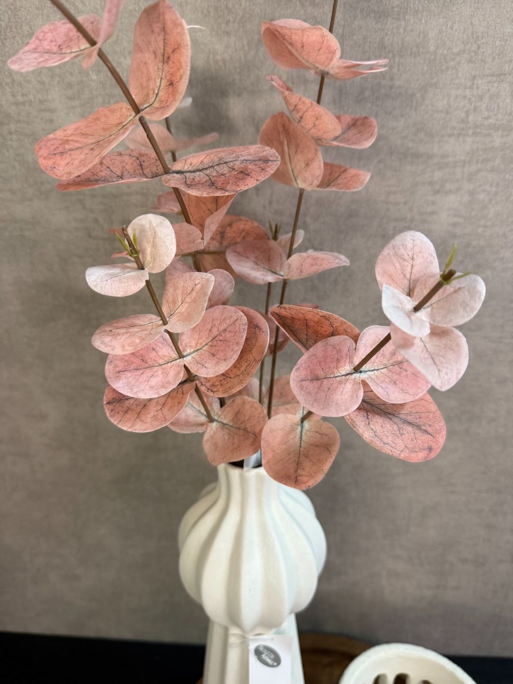 Ronde houten tray met crème vaas met roze kunsttakken en twee crème waxinelichthouders op een zwarte tafel.