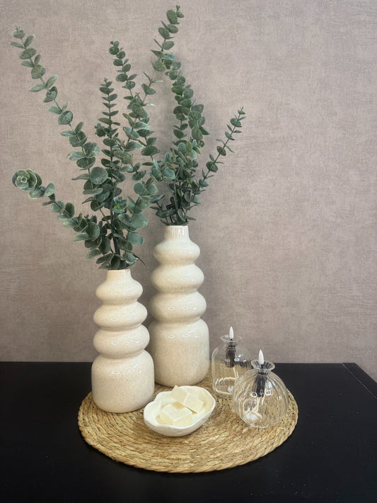 Tafel decoratie set Lovi – beige vazen met eucalyptustakken, LED-oliekaarsjes en amberblokjes op gevlochten placemat.