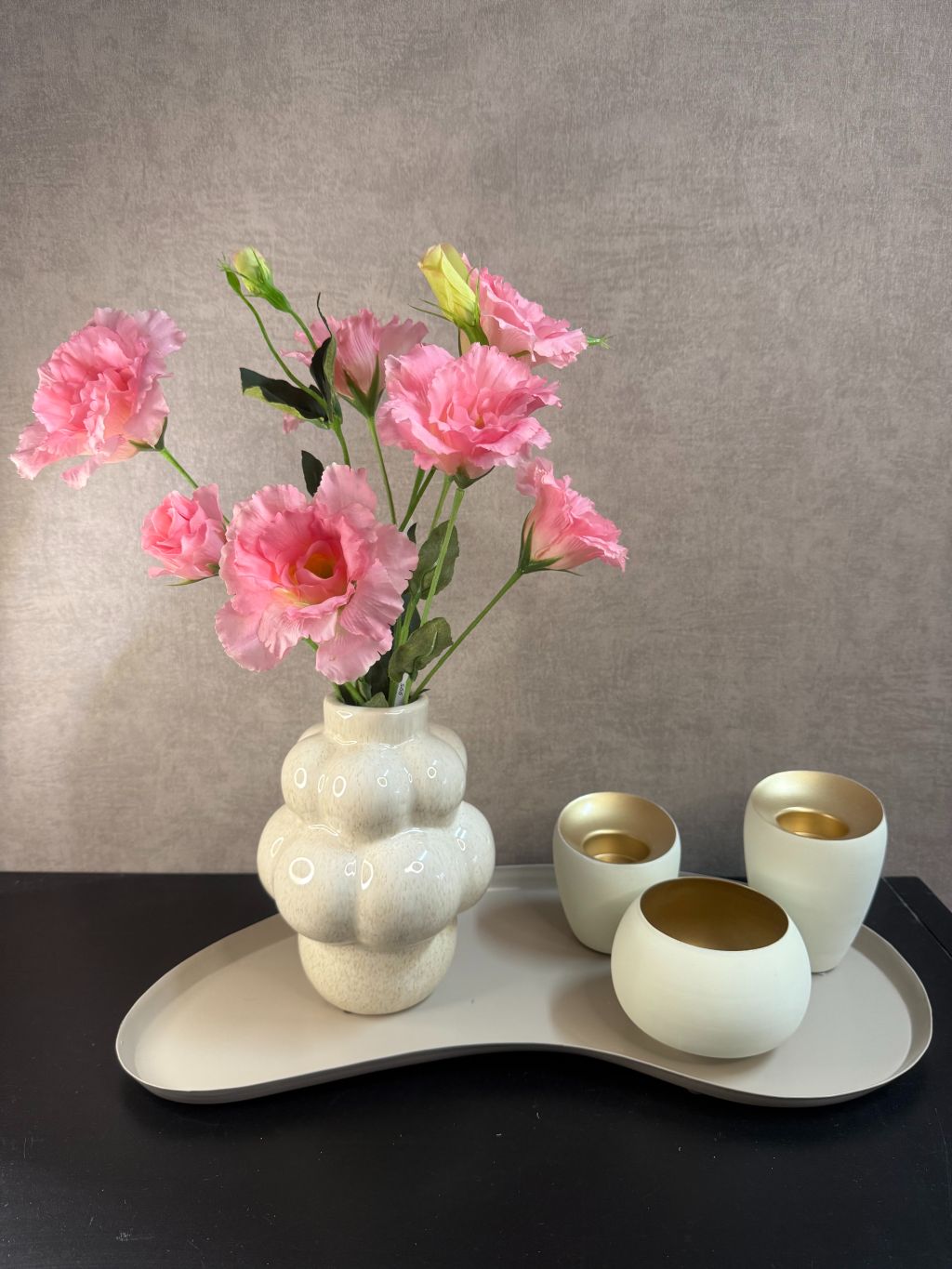 Decoratieve set met roze kunstbloemen in organische vaas en drie theelichthouders op zandkleurig dienblad.