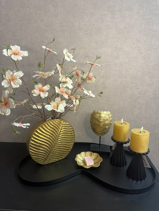 Tafelstyling met zwart dienblad, gouden accessoires, roze bloesemtakken en amberblokje als complete decoratieset.