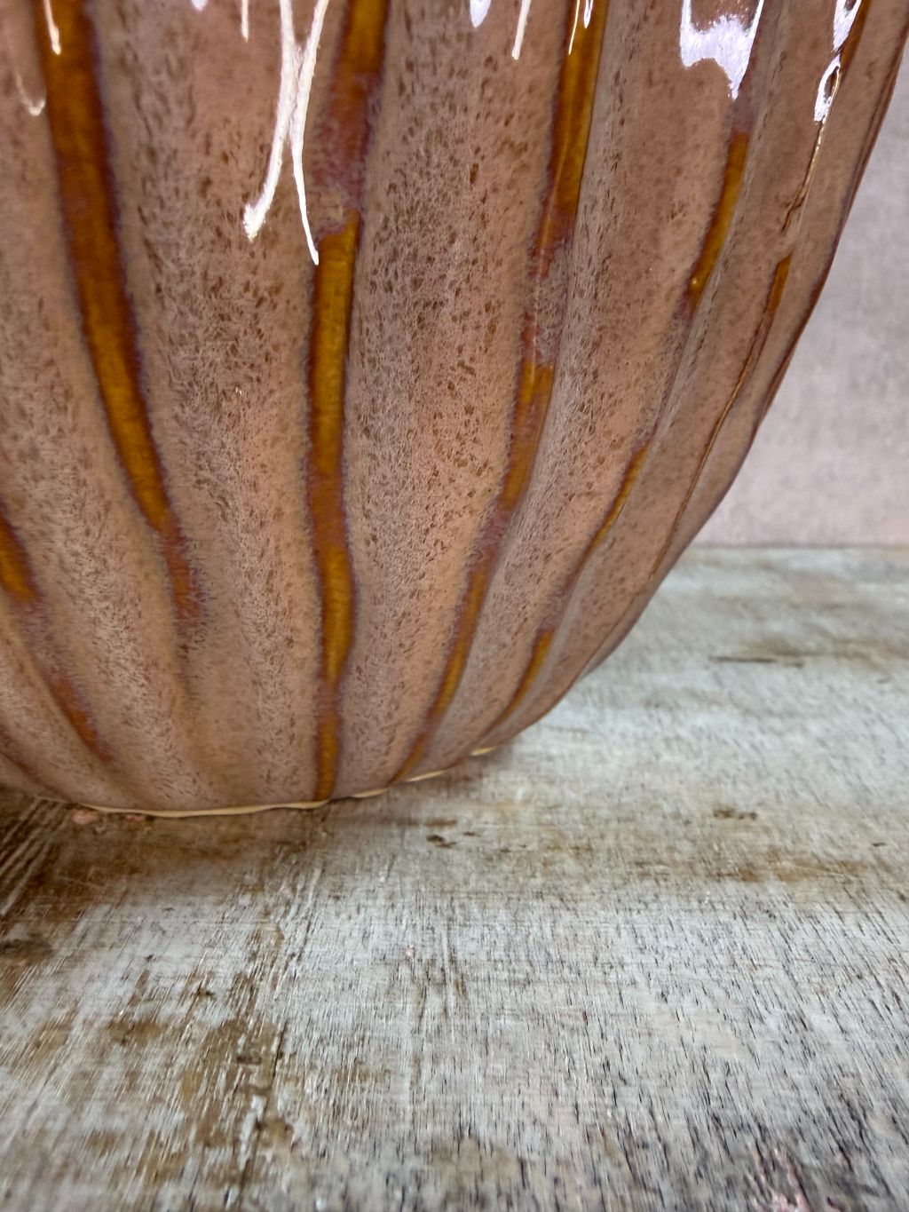 Keramieken vaas in oudroze en bruin met verticaal reliëf en glanzende afwerking, geplaatst op een houten ondergrond.