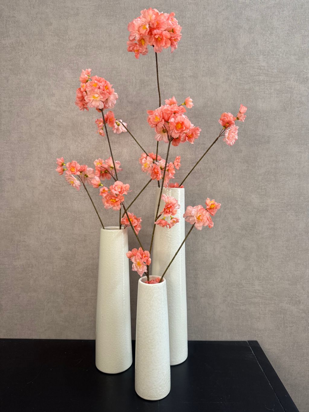 Drie crèmekleurige vazen van keramiek met kunstbloemen in verschillende hoogtes en smalle cilindervorm, staand op een houten oppervlak.